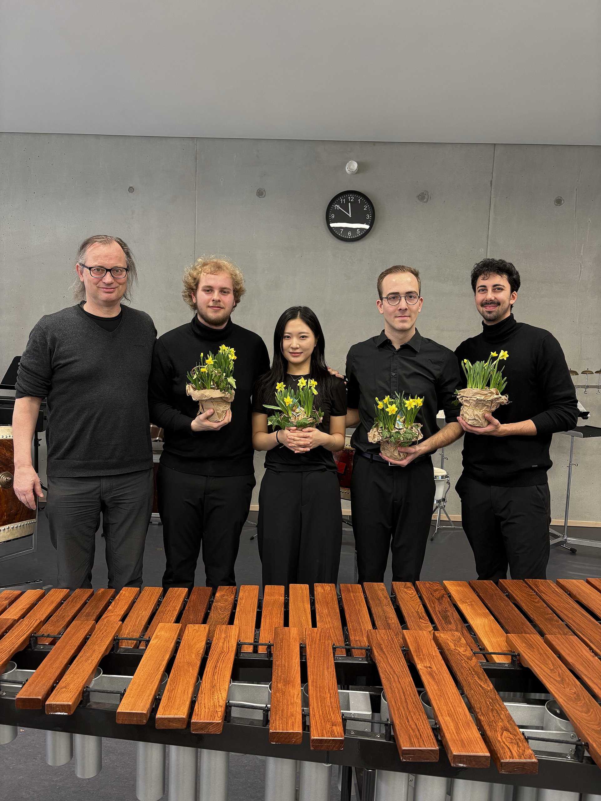 Alle vier Musikstudenten halten Blumensträuße und stehen hinter der Marimba. Rechts neben ihnen steht ihr Lehrer