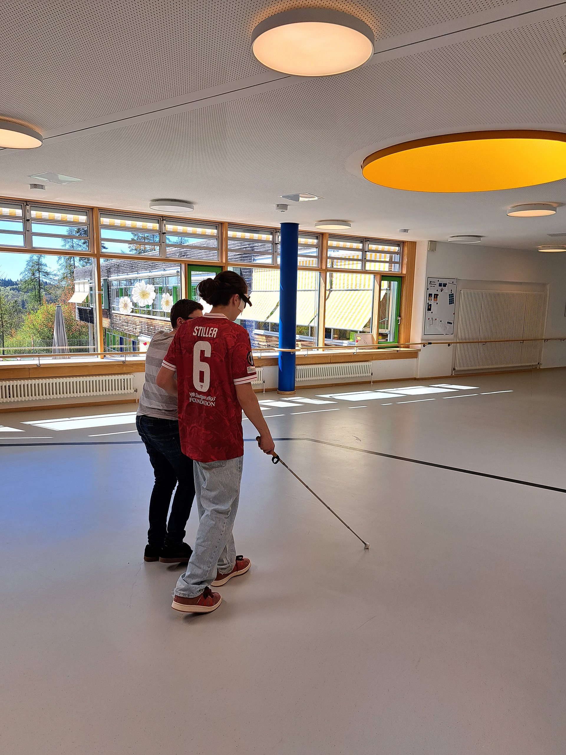 Zwei Schüler laufen über den Schulgang. Einer trägt eine Augenbilde und läuft mit einem Langstock