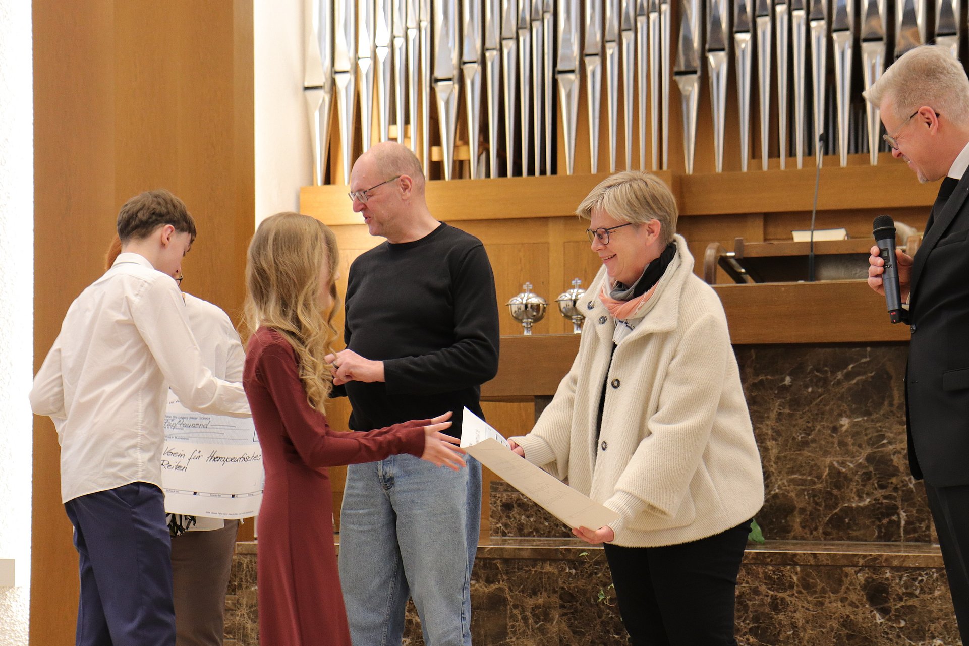 Jugendliche überreichen Erwachsenen Spendenschecks. Sie stehen in einer Kirche vor einem Altar. Im Hintergrund ist eine Orgel zu sehen