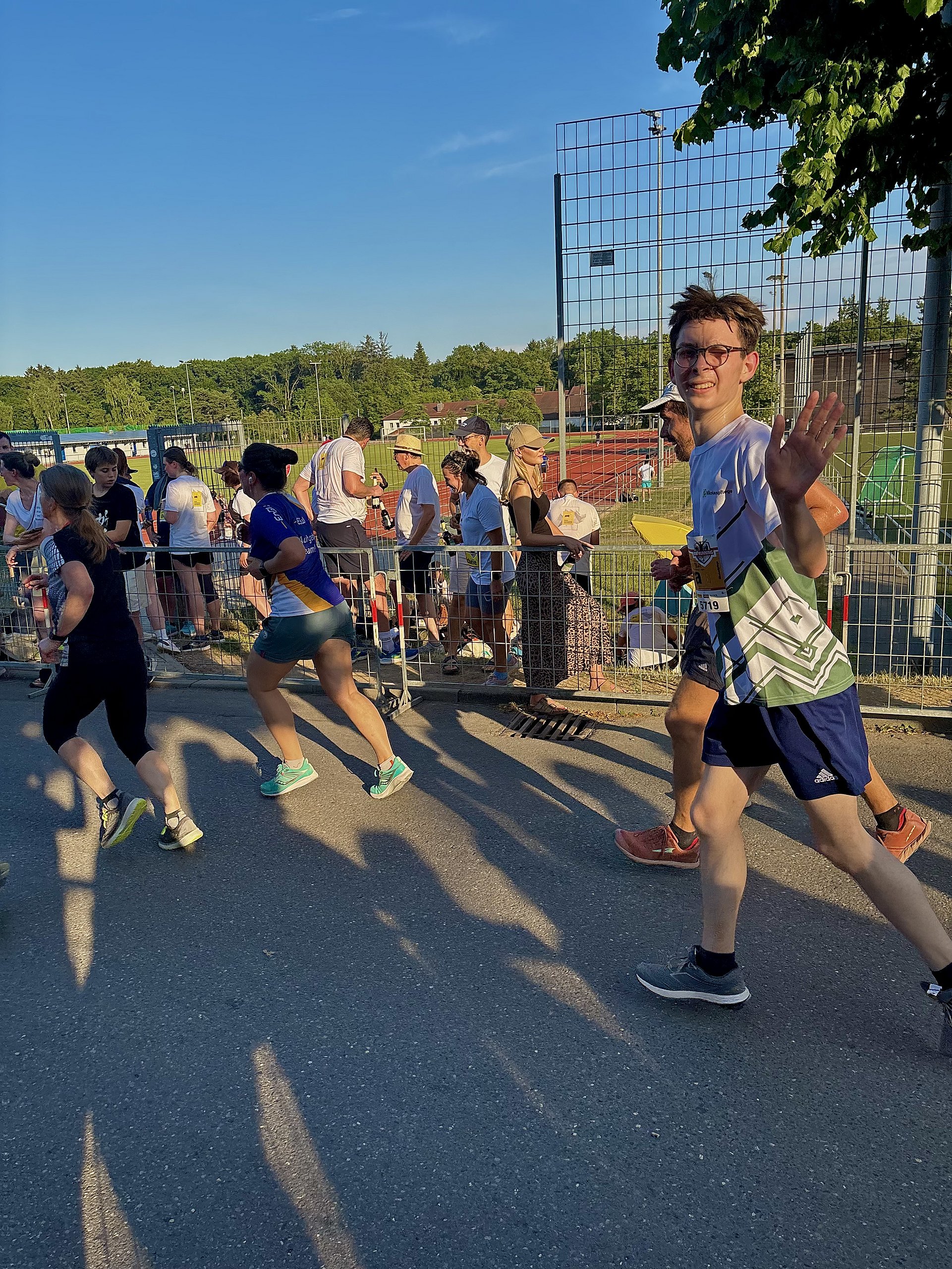Bei einem Wettlauf auf einer Straße rennen viele Personen in Sportbekleidung nebeneinander. Ein Mann winkt mit beiden erhobenen Armen