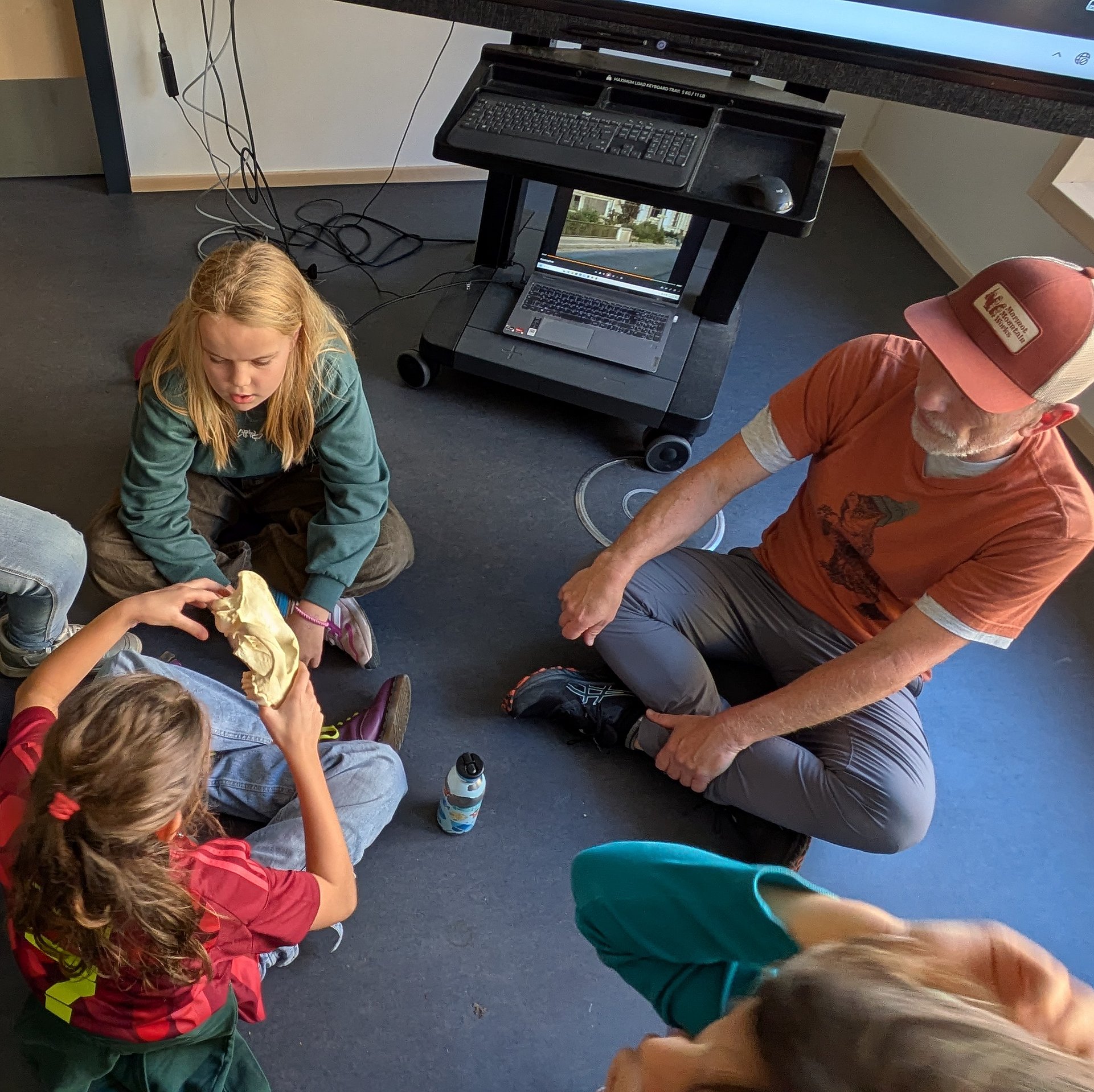 Schülerinnen und Schüler sitzen im Klassenraum auf dem Boden in einem Kreis