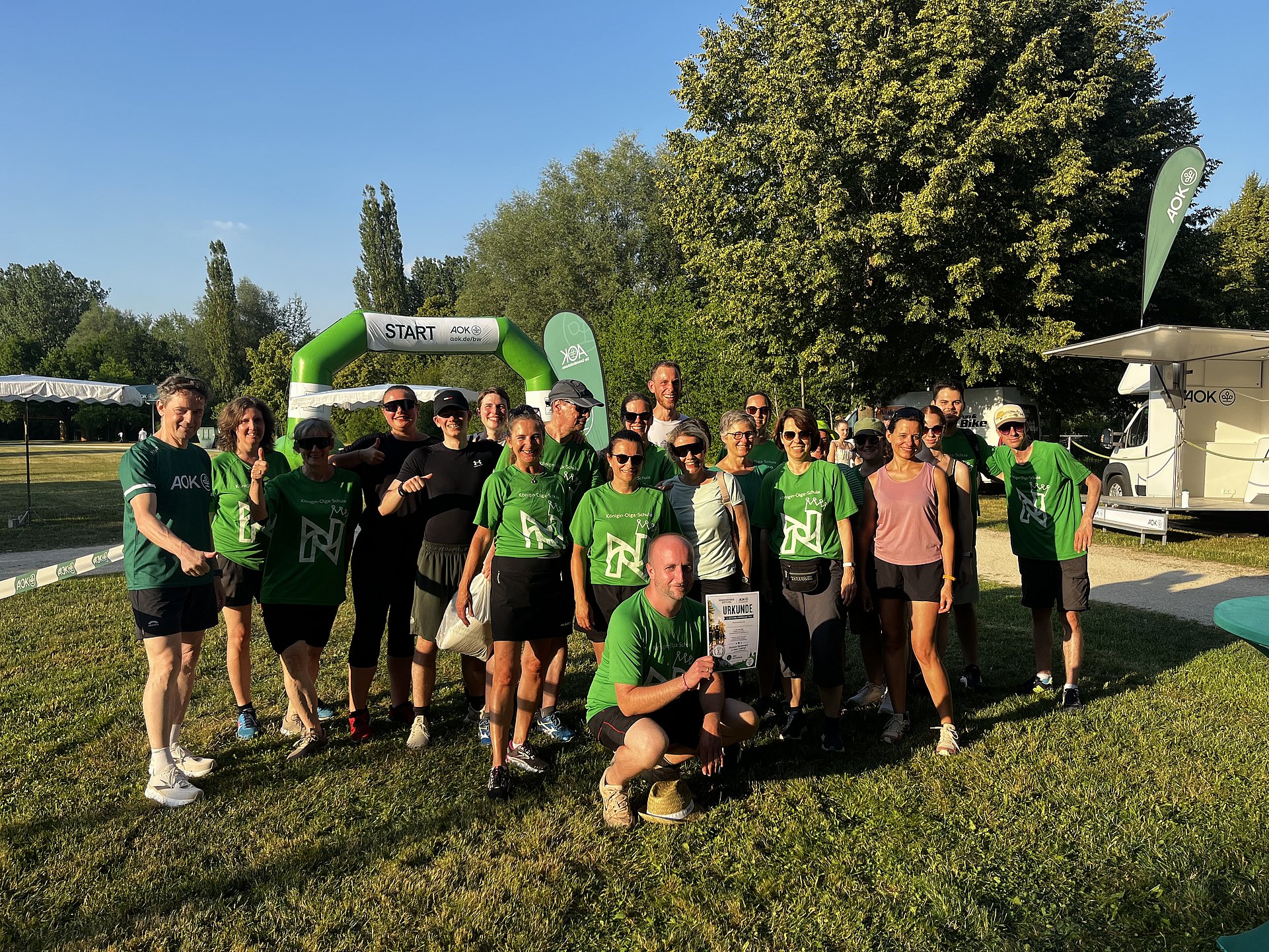 Eine größere Gruppe von Menschen in Sportkleidung auf einer Wiese bei einer Laufveranstaltung.