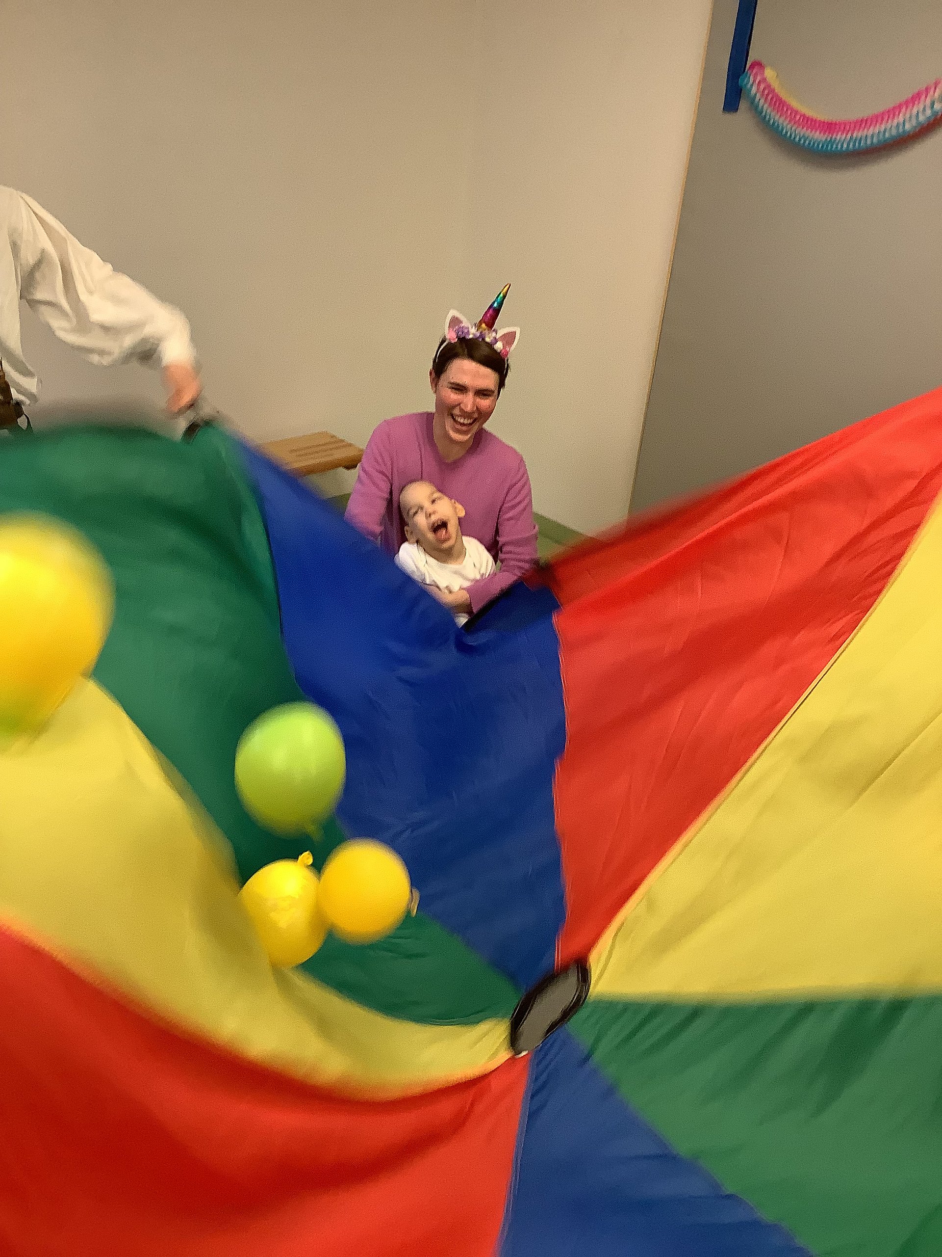 Eine Betreuerin und ein Kind halten gemeinsam ein großes buntes Tuch, darin fliegen bunte Bälle
