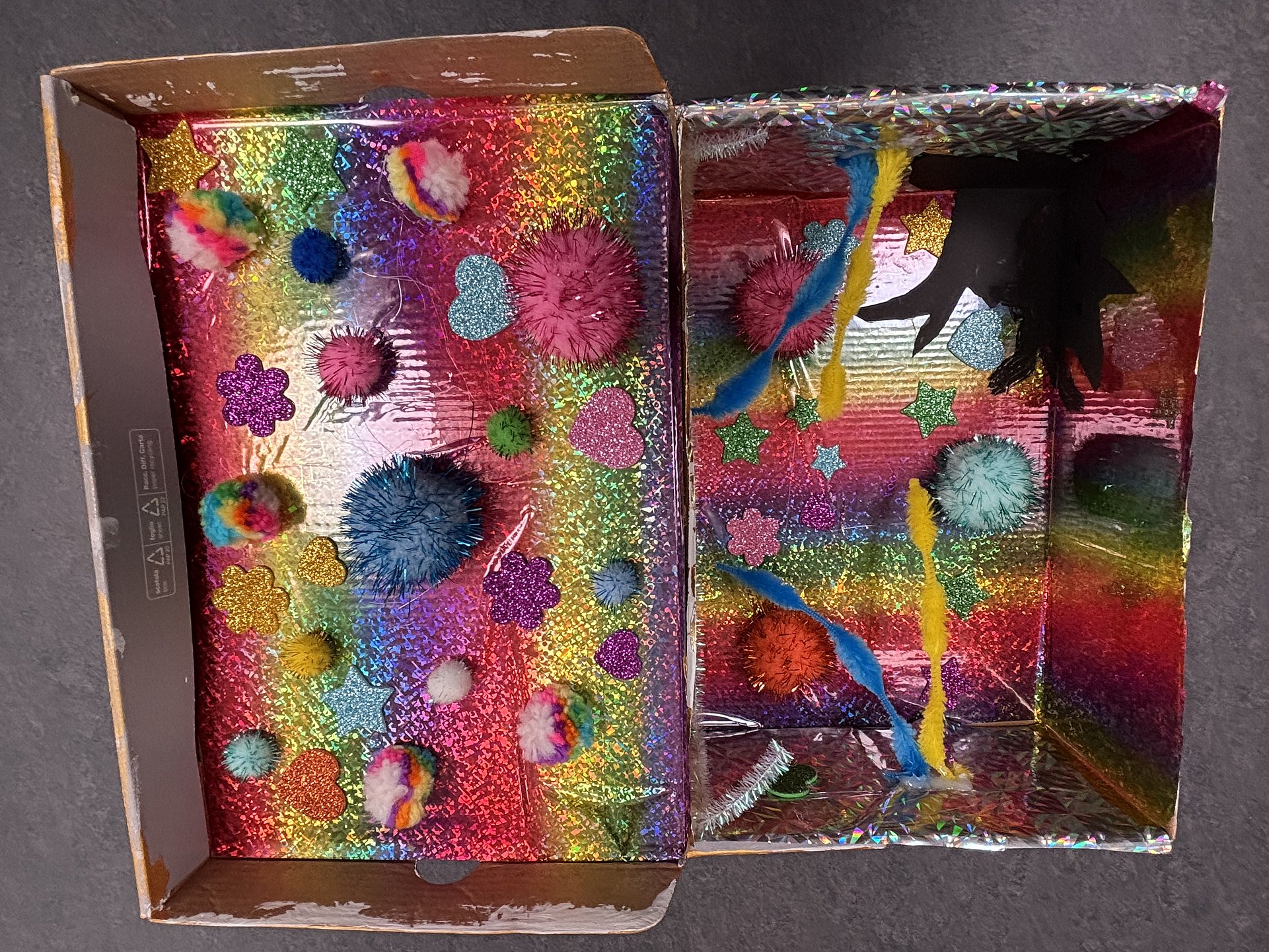 Ein bunt gestalteter Pappkarton mit glitzernden Farben und verschiedenen Dekoelementen