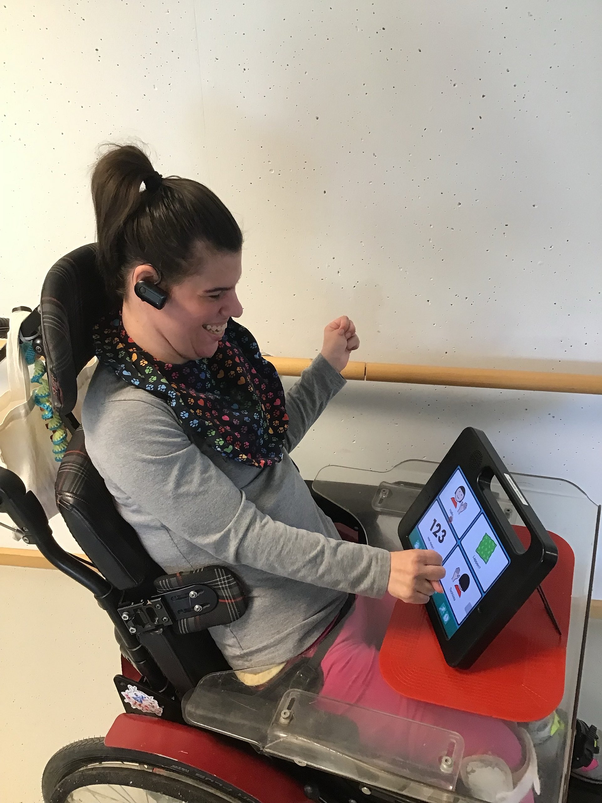 Eine Klientin sitzt im Rollstuhl und bedient ein Tablet, das vor ihr auf dem Tisch steht