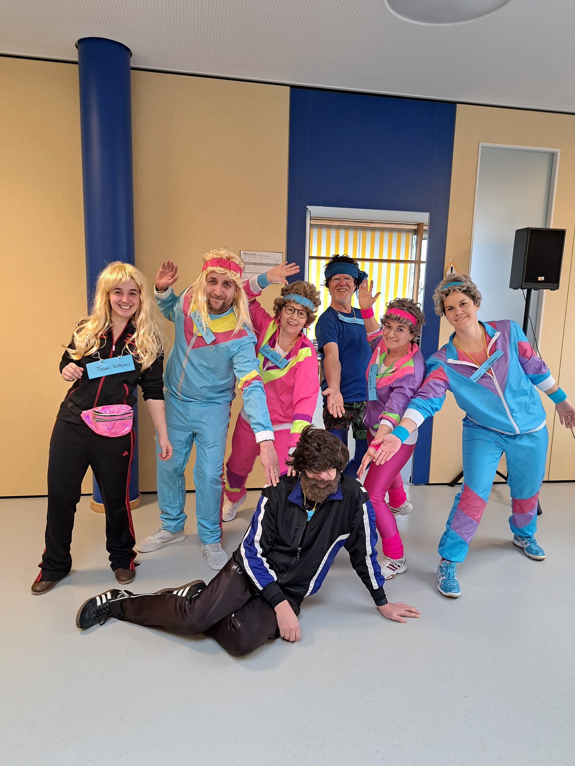 Eine Gruppe von Mitarbeitenden hat sich zu Fasching mit Trainingsanzügen verkleidet
