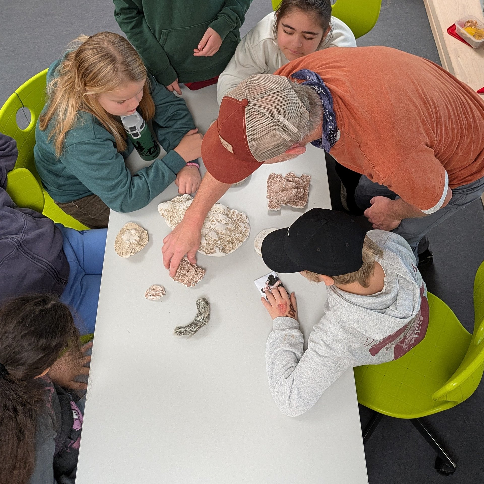 Schülerinnen und Schüler sitzen an einem Tisch im Klassenraum und arbeiten mit Unterrichtsmaterial