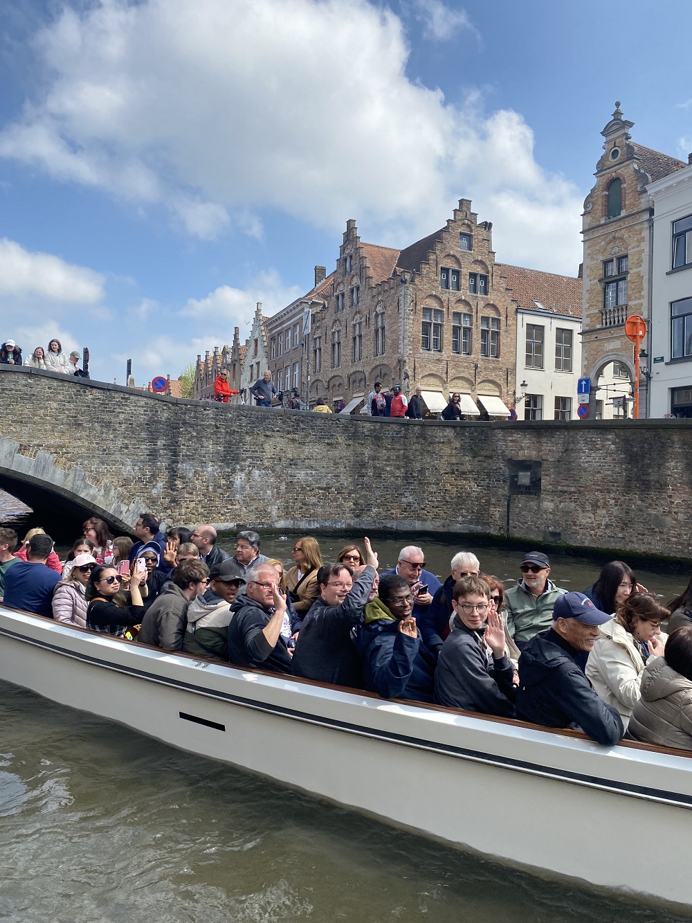 Eine Gruppe junger Erwachsener sitzt in einem Boot. Es fährt auf dem Wasser einer Gracht in der belgischen Stadt Brügge