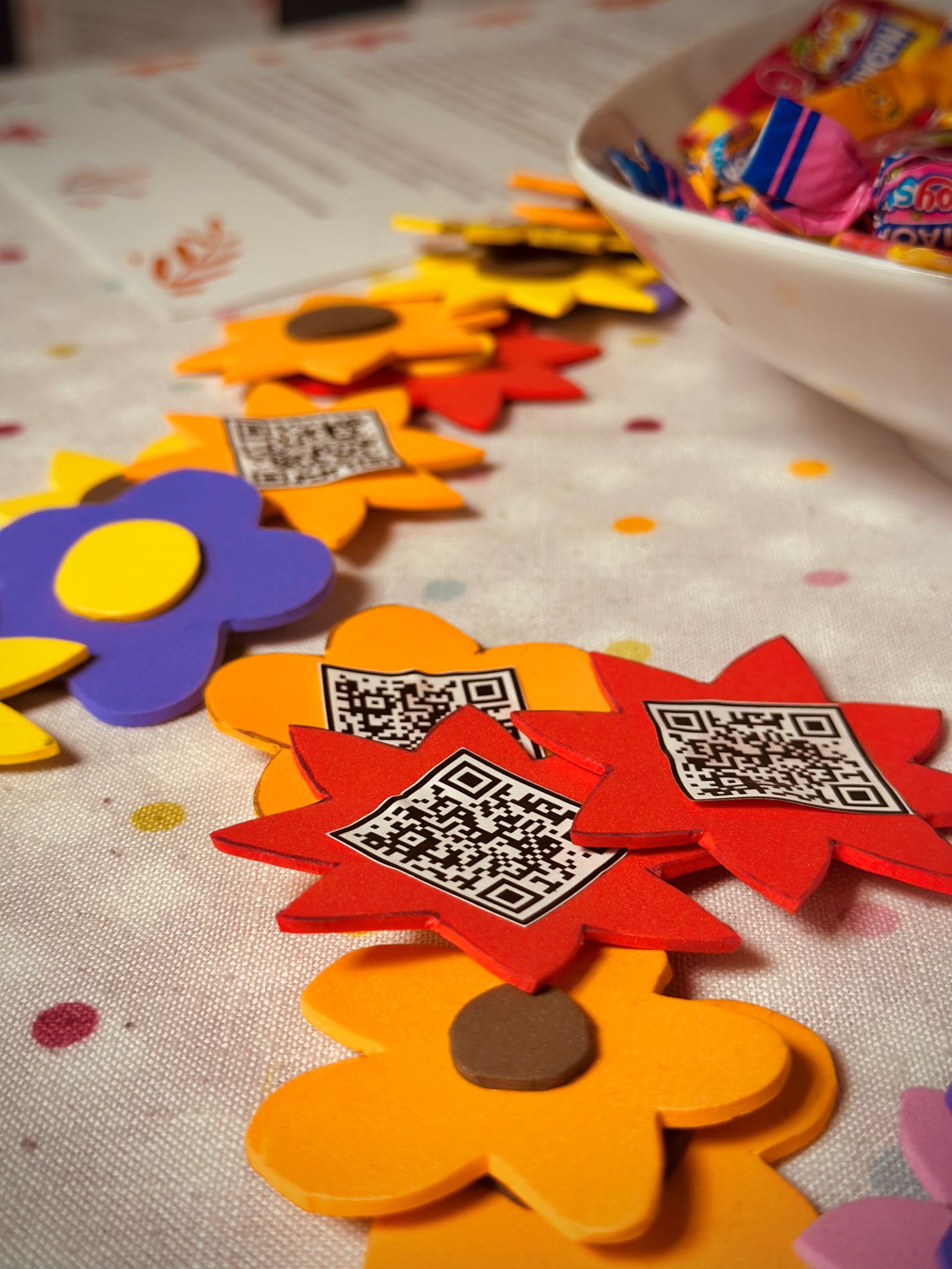 Auf einem Tisch liegen ausgeschnittene Formen in verschiedenen Farben, zum Beispiel Sterne und Blumen. Auf einigen klebt ein QR Code
